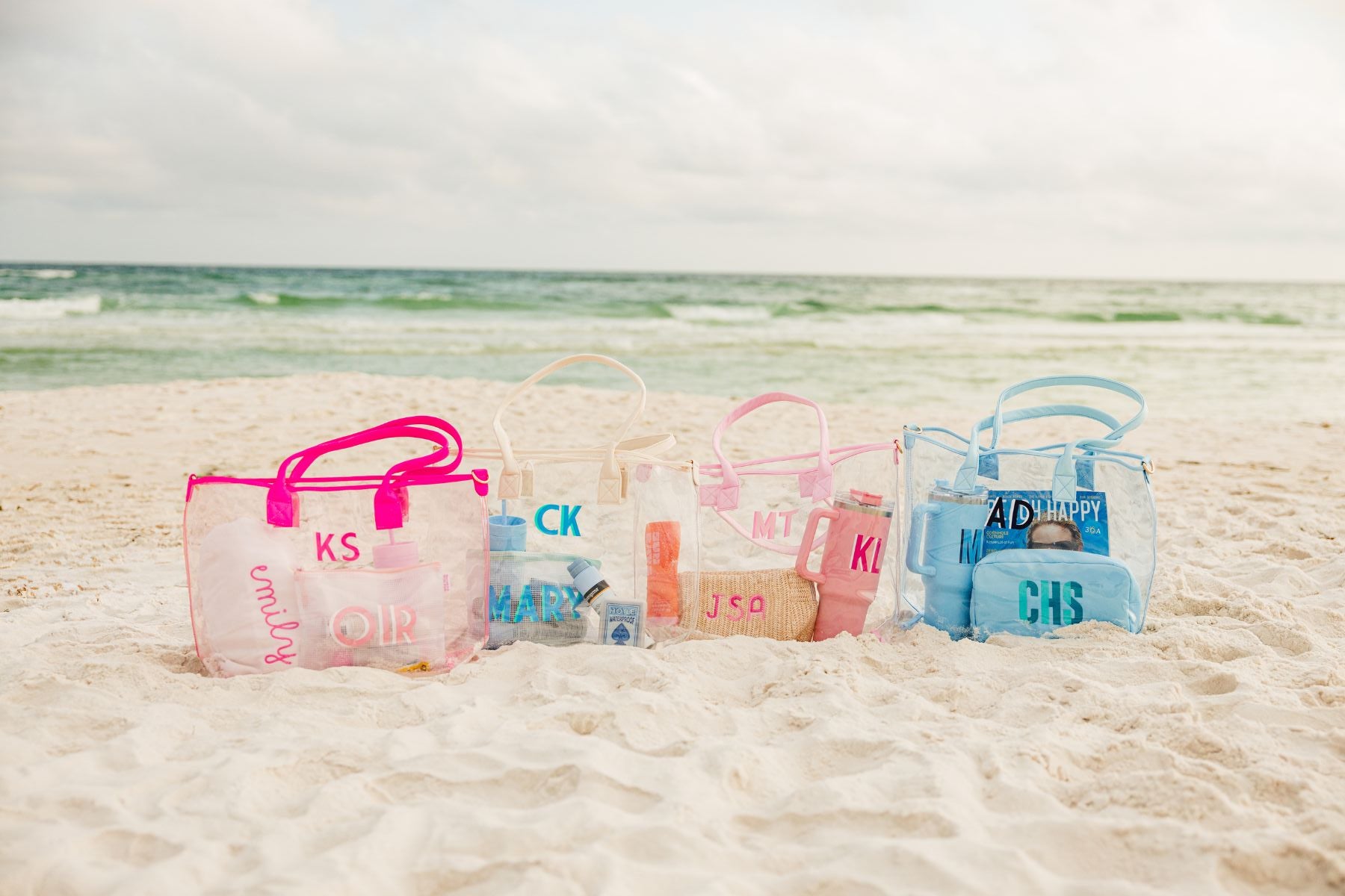 A white, pink, and a blue clear tote are personalized with different colored monograms.