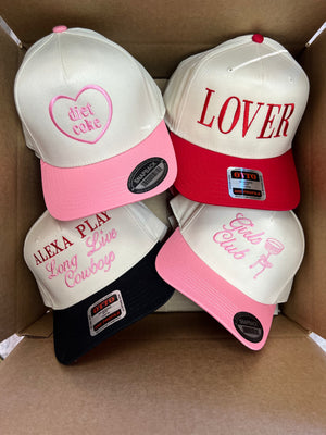 Box containing a vibrant set of personalized trucker hats, including the featured 'Diet Coke' heart design in pink and red embroidery, alongside other bold and stylish text designs. A perfect collection for gifting or coordinating group events.