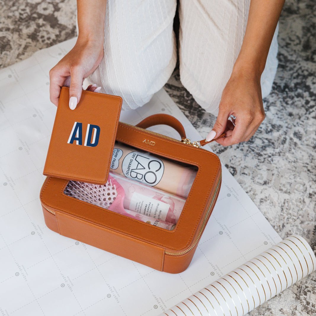 A group of white, tan, and black train cases are personalized with gold foil monograms.