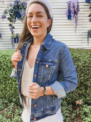 A woman in a headband stands outside showing off the fit of her custom jean jacket.