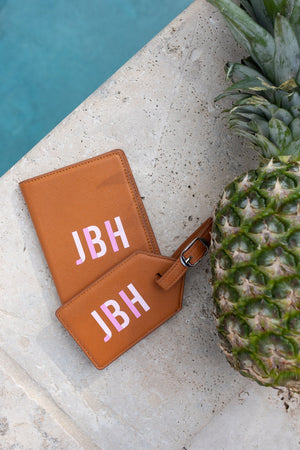 A tan passport holder and leather pouch are customized with a pink monogram