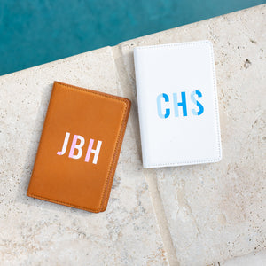 A white and a tan passport holder are customized with colorful monograms