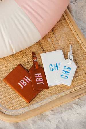 A tan passport and luggage tag set and a white passport holder and luggage tag set are customized with monograms.