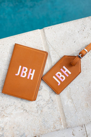 A tan passport holder and leather pouch are customized with a pink monogram