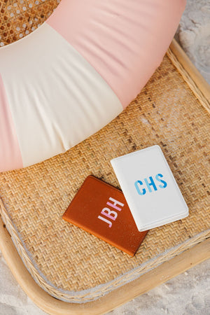 A tan passport holder is personalized with a pink monogram and a white passport holder is personalized with a blue monogram