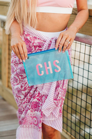 A girl on a boardwalk holds up a blue pool bag with a two toned pink monogram.