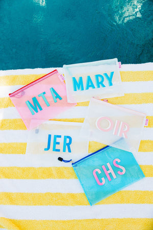 A group of pool bags are customized with colorful monograms by the pool.