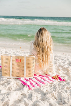 A girl sits on the beach with a canning tote that has been customized with a pink and orange monogram