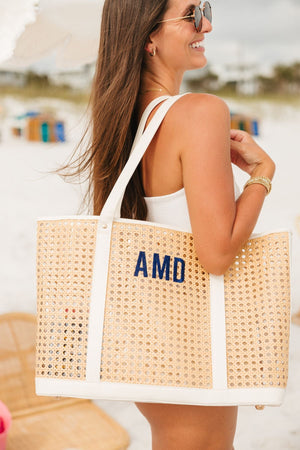 A girl smiles at the beach holding her canning tote with a navy embroidered cane tote.