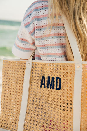 A girl in a striped shirt holds a canning tote with a navy embroidered monogram.