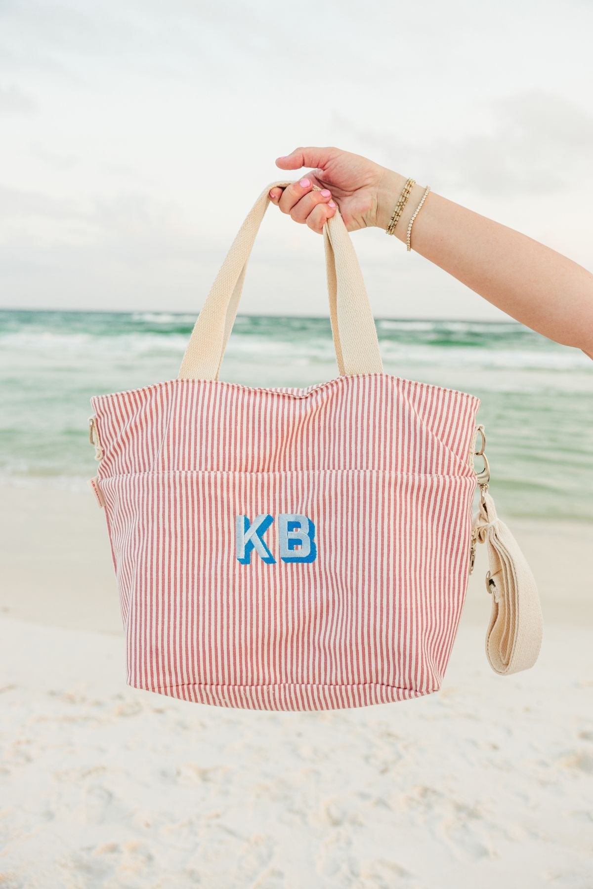 A monogrammed pink and navy stripped cooler tote are filled with snacks and drinks.