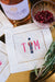 A square cocktail napkin is customized with an embroidered nutcracker surrounded by a pink monogram.