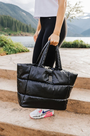 A woman walks down some steps holding her puffer tote which is embroidered with her initials.