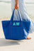 A cream, pink, and blue tote are personalized with embroidered monograms and names.