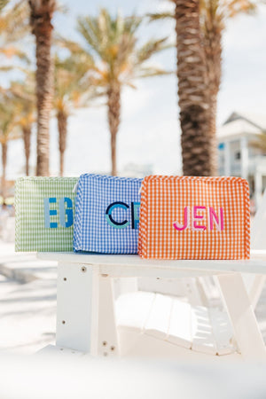 A green, blue, and an orange roadie are embroidered with colorful monograms and placed on a beach chair.