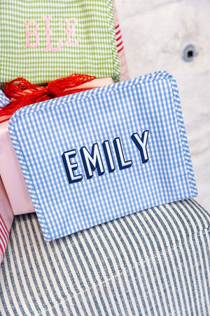 A blue gingham pouch is embroidered with a name in white and navy thread.