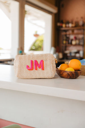 A straw pouch is customized with a pink and orange monogram and placed on the counter.