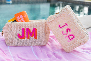 Two straw pouches are customized with pink monograms on a pink towel