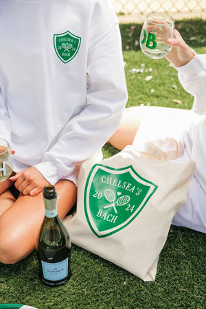 A girl wears a white Last Swing Before The Ring sweatshirt and sits next to a tote bag with the same design.