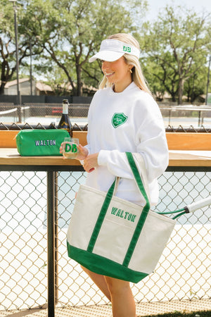 A girl wears a white Last Swing Before The Ring sweatshirt and holds a variety of other monogrammed products at a tennis court