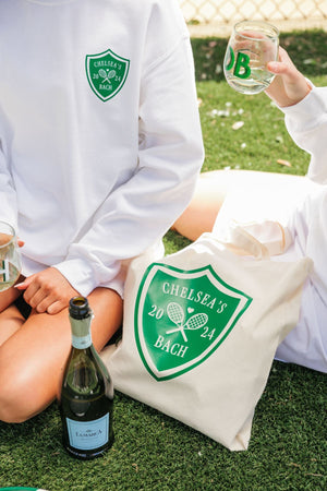 A girl wears a white Last Swing Before The Ring sweatshirt and sits next to a tote bag with the same design.