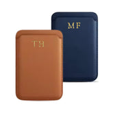 Two sleek leather phone wallets displayed side by side. The left wallet is in a rich tan color with 'HLF' monogrammed in gold, while the right cover is navy blue with 'AL' also in gold. Both items exhibit a smooth finish and precise stitching, showcasing a blend of practicality and personalized elegance.