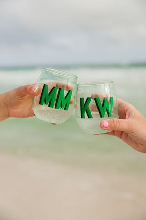 Two people on the beach cheers with green monogrammed wine glasses.