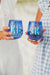 Two people cheers with their blue monogrammed wine glasses.