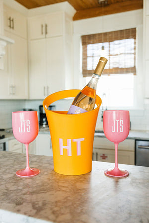 An orange ice bucket is placed on the counter next to a set of pink wine glasses