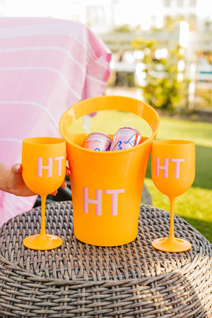 An orange wine bucket and 2 orange wine glasses are customized with a pink monogram