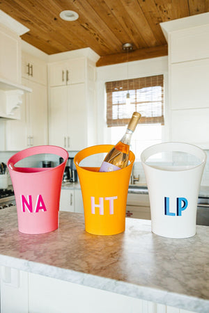 A pink, orange, and a white ice bucket are customized with monograms.