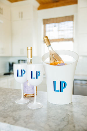 A white ice bucket and 2 white wine glasses are customized as a set with blue monograms