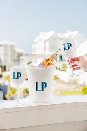 A white ice bucket with a bottle of wine is placed next to a set of white wine glasses with a matching blue monogram.