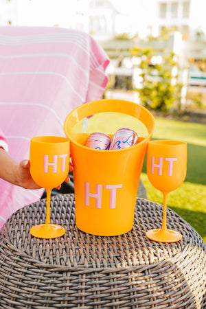 An orange wine bucket and 2 orange wine glasses are customized with a pink monogram