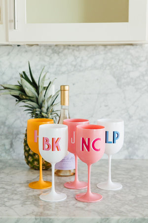 A group of pink, orange, and white wine glasses are monogrammed with different colors.