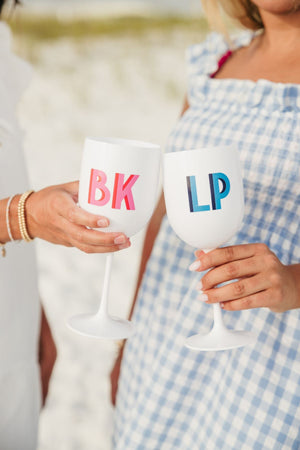 Two girls cheers with white wine glasses with a pink and blue monogram.