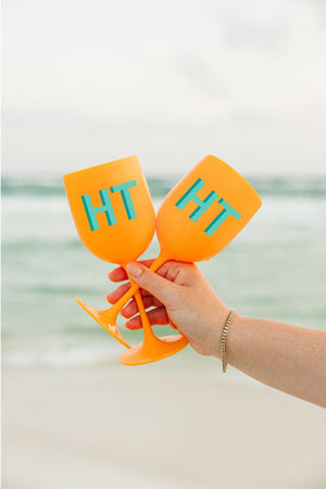 A person holds a set of orange wine glasses with a mint and turquoise monogram.