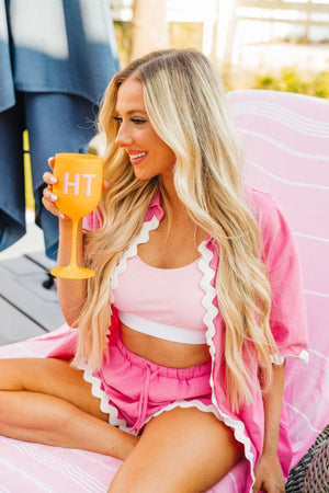 A girl sits outside enjoying a drink in her orange monogrammed wine glass