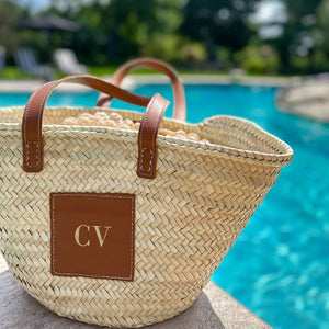 Close-up of a personalized straw tote bag with leather handles and 'CV' initials in gold