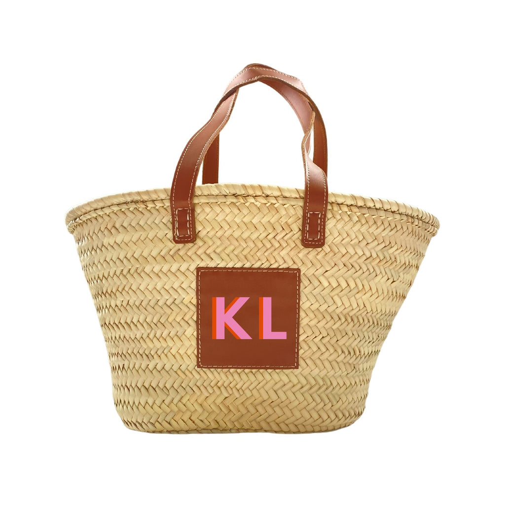 A straw tote is customized with a pink and orange monogram.