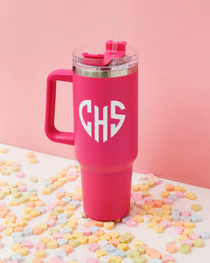 A bright pink tumbler is customized with a white heart monogram