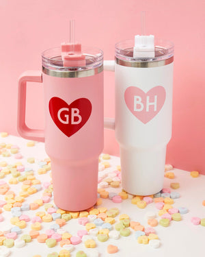 A pink and white tumbler are customized with heart monograms