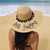 A girl sits on the beach wearing a custom pom pom floppy beach hat reading "Mrs. Lawson."