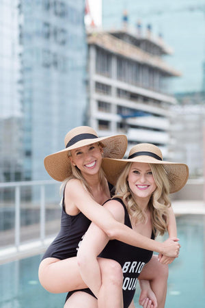 Two women wear custom black swimsuits and matching custom black ribbon floppy hats.