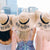 Three women cheers their champagne flutes while wearing customized black ribbon floppy beach hats