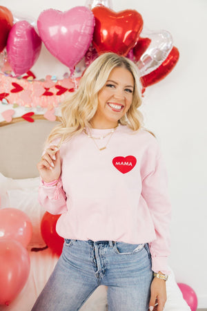 A woman wears a pink sweatshirt decorated with a red heart that reads "Mama"