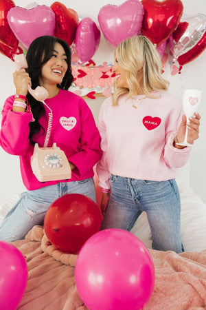 Two women laugh together wearing their pink customized sweatshirts for Valentine's Day