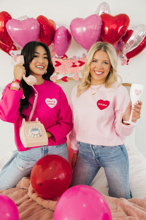 Two women laugh together wearing their pink customized sweatshirts for Valentine's Day