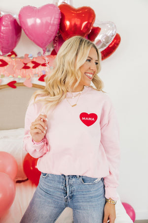 A woman wears a pink sweatshirt decorated with a red heart that reads "Mama"