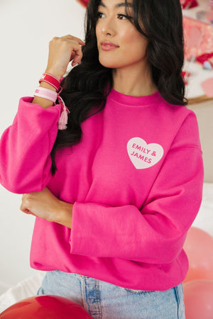 A woman shows off her bright pink sweatshirt personalized with "Emily & James" in a heart.